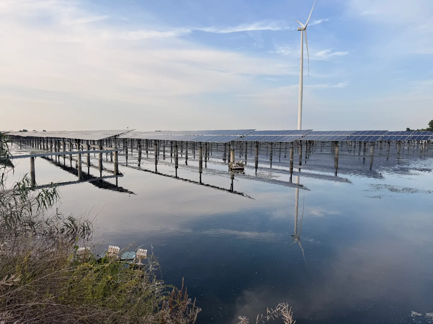 Solar tracker installation over water with a wind turbine